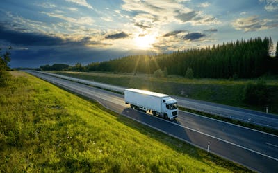 White Tractor Trailer driving on empy highway in Oregon forest with Oregon truck weight distance permit